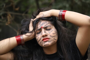 A southeast Asian brown woman protesting gender based violence by writing anti violence against women and girls messages all over her face and looking angry and sad