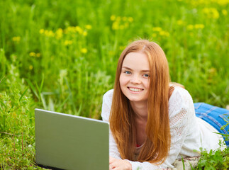 girl working in nature with a laptop lying on the green grass. The girl works as a freelance traveler.