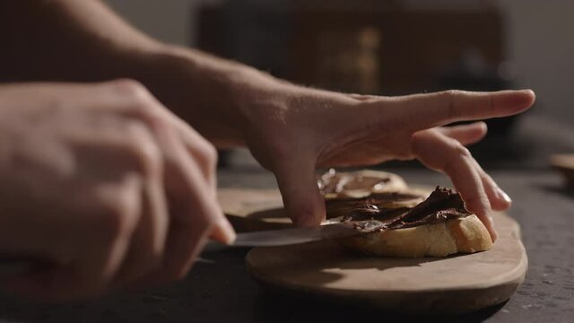 Man spreading chocolate hazelnut cream on baguette slice on olive board