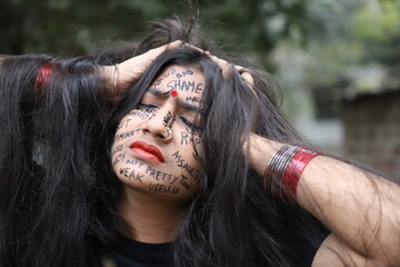 A southeast Asian brown woman protesting gender based violence by writing anti violence against women and girls messages all over her face-vertical conceptual photograph 