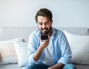 Smiling Arab Man Recording Voice Message On Smartphone Or Using Virtual Assistant