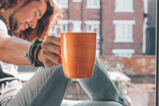 Caucasian offering his coffee mug while looking other side