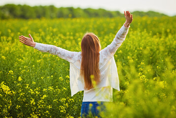 Naklejka na ściany i meble woman with open arms in the green rapeseed field.