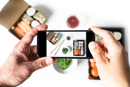 Top view of man taking photo of sushi on the white table. Social networking and take-away concept