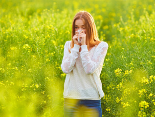 Allergic to pollen and flowering season, a redhead girl sneezing on a field