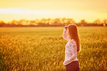 Young woman standing on a wheat field with sunrise