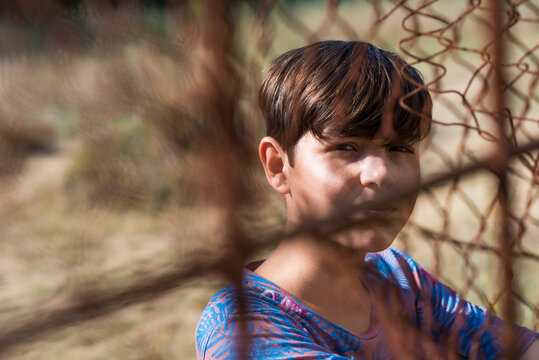 serious teen in casual wear behind metallic fence outdoors