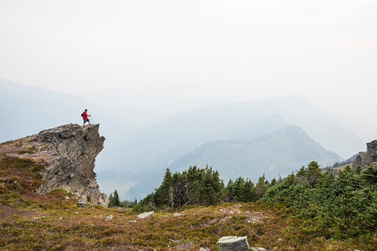 Full length of hiker standing on cliff against mountains and sky during foggy weather
