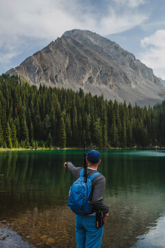 Rear view of hiker with backpack pointing towards lake while standing against mountains at forest