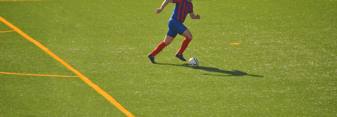 Jogador a correr isolado com a bola na direção da baliza na entrada da grande área - campo de treinos com relva artificial - equipamento em cores azul e vermelho