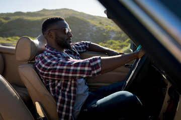 African american man driving on sunny day in convertible car holding driving wheel