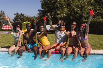 Diverse group of friends drinking beer and sitting at the poolside