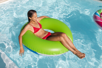 Mixed race woman having fun playing on inflatable in swimming pool