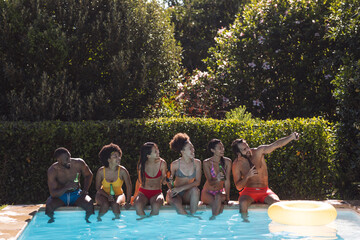 Diverse group of friends drinking beer and sitting at the poolside talking