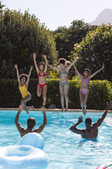 Diverse group of female friends jumping into water at a pool party