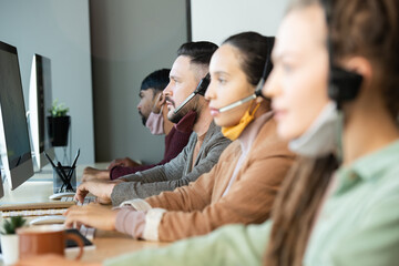 Serious male operator with protective mask under chin consulting clients online