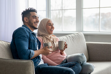 Beautiful muslim couple drinking tea, looking at copy space