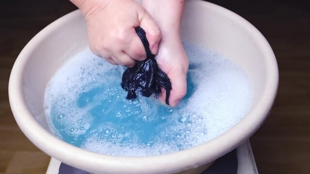 woman washes with her hands blue men's panties in a basin, knitted underwear, clean clothes concept, scandal in the Russian Federal Security Service