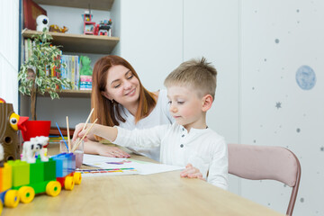young mother draws teaches her little son to draw, in the nursery at home, having fun together