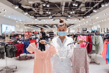 Young woman shopping apparels in clothing boutique with protective face mask