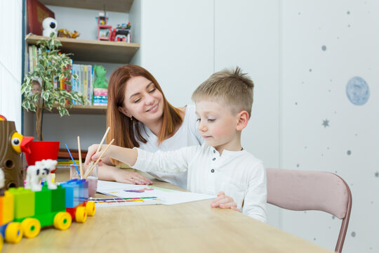 young mother draws teaches her little son to draw, in the nursery at home, having fun together