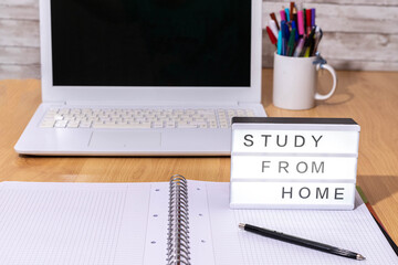 selective focus of a study table with a notebook, pens and a laptop computer together with a light box indicating Home Study in covid19 time confinement with concept of health