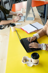 Hands of two young co-workers in casualwear sitting by table and typing