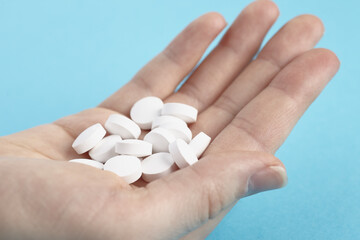 Closeup of white pills on a hand on a blue background. Heap of pills - medical background