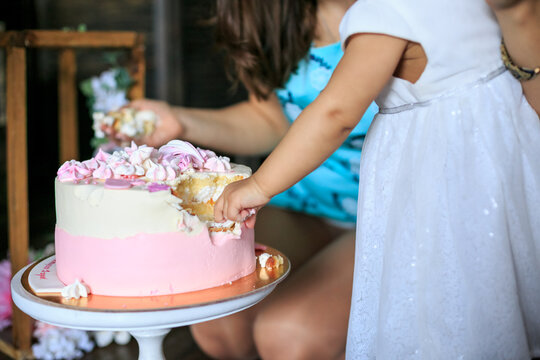 Close up shot of baby girl hand destroys pink cake. Birthday party celebration. First year, childhood, people concept. Making messy cake smash, crem. Childrens holiday. First baby birthday
