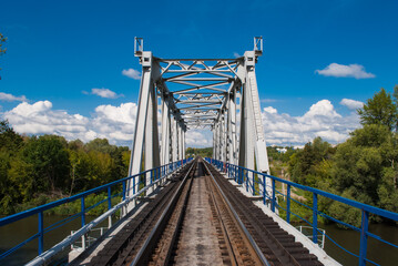 Railroad bridge view on background with green trees and blue cloudy sky