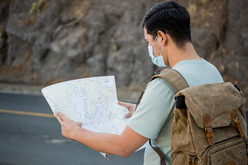 Viajero masculino con una mochila y mapas con una máscara sanitaria de pie en la carretera