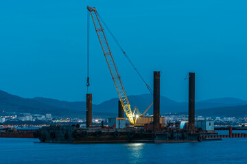 Obraz premium Cargo crane working in small port, construction of industrial harbor or dock in evening, sea goods transportation and logistic development concept.