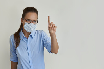 Woman in medical face mask and blue shirt pointing her finger to a blank space