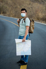 Viajero masculino con una mochila y mapas con una máscara sanitaria de pie en la carretera