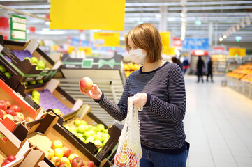 Young woman wearing protective medical face mask shopping in supermarket during coronavirus pneumonia outbreak.
