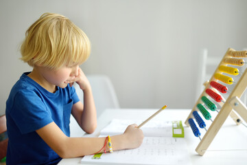Elementary student boy doing homework at home. Child learning to count, solves arithmetic examples,...
