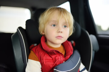 Portrait of a preschooler boy sitting in a car seat and wearing a belt. Сhild bored during a family trip. Safety of children in transport.