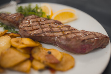 Pepper or mustard steak, grilled on a plate and served with some baked potatoes on a plate in a restaurant. Delicious meal served on a white plate.