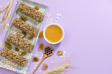 Fresh homemade granola bars with raisins, homey and oat flakes on light violet background. Healthy diet food concept.