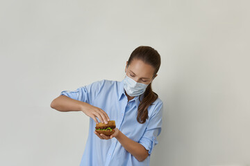 Beautiful young woman in the medical mask holding in her hand and cooking a tasty vegan burger. The concept of vegan fast food