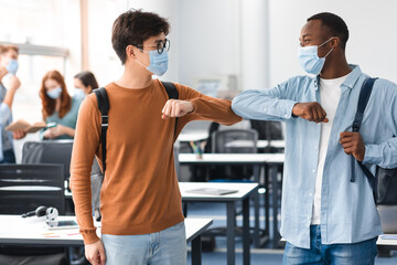 Fototapeta na wymiar Diverse students wearing face masks greeting and bumping elbows