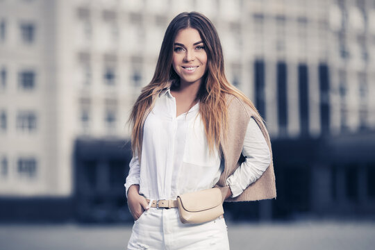 Young fashion woman in white shirt and jeans walking on city street