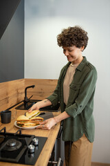 Happy young brunette female in casualwear putting homemade sandwiches on plate