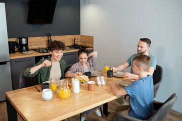 Fototapeta na wymiar Happy family of four sitting by served wooden dinner table in the kitchen
