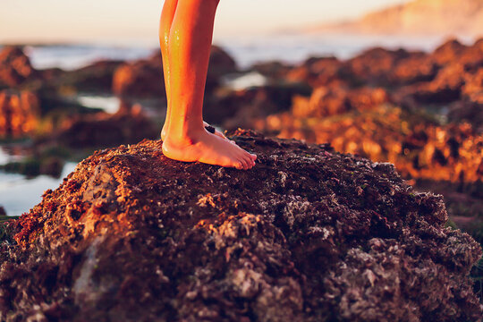 Boy standing on a rock at the beach at low tide, focus on feet. - Powered by Adobe