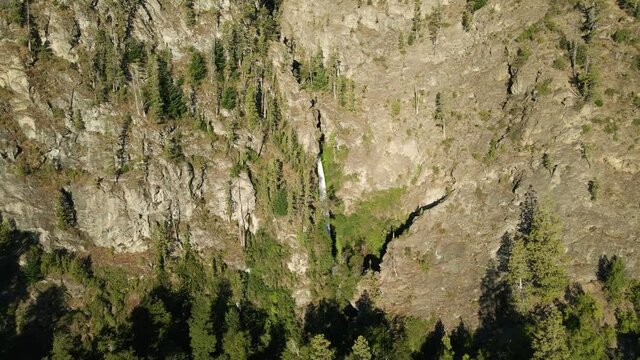 Aerial dolly out of Corbata Blanca thin waterfall falling between mountains with pine trees, Patagonia Argentina