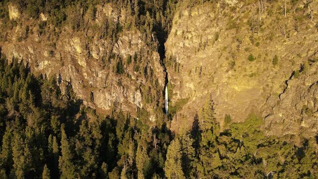 Aerial rising over Corbata Blanca thaw waterfall hiding between mountains surrounded by pine trees at sunset, Patagonia Argentina