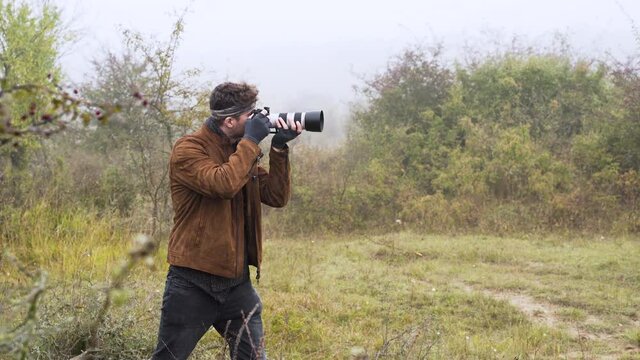 Wildlife photographer with a DSLR camera taking photos in bushes,mist.