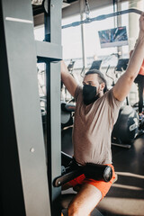 Fototapeta premium An active man in a protective medical mask training in gym. Sport and quarantine.