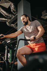 Fototapeta na wymiar An active man with beard training in gym, riding a stationary exercise bike. Sport and quarantine.